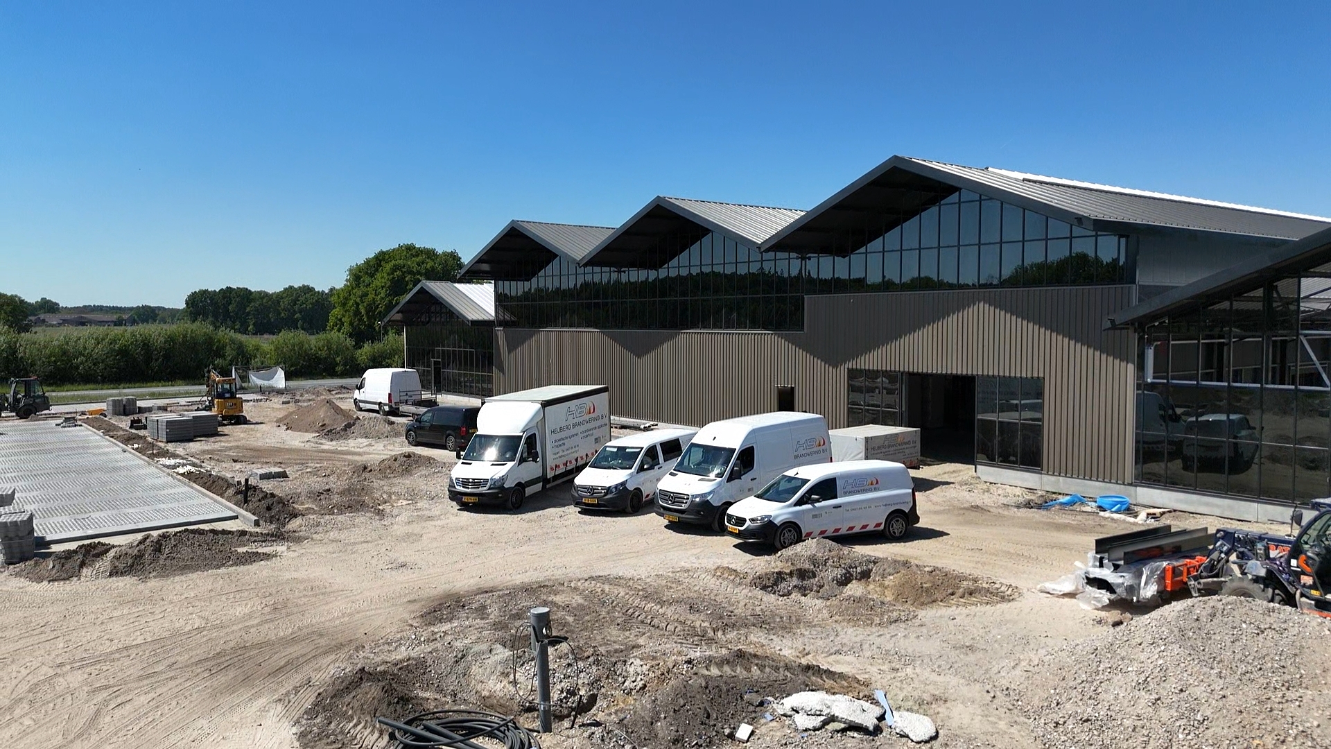 Industrieel gebouw met bedrijfswagens op bouwterrein.